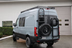 Van with roof rack and ladder on a driveway in front of a garage