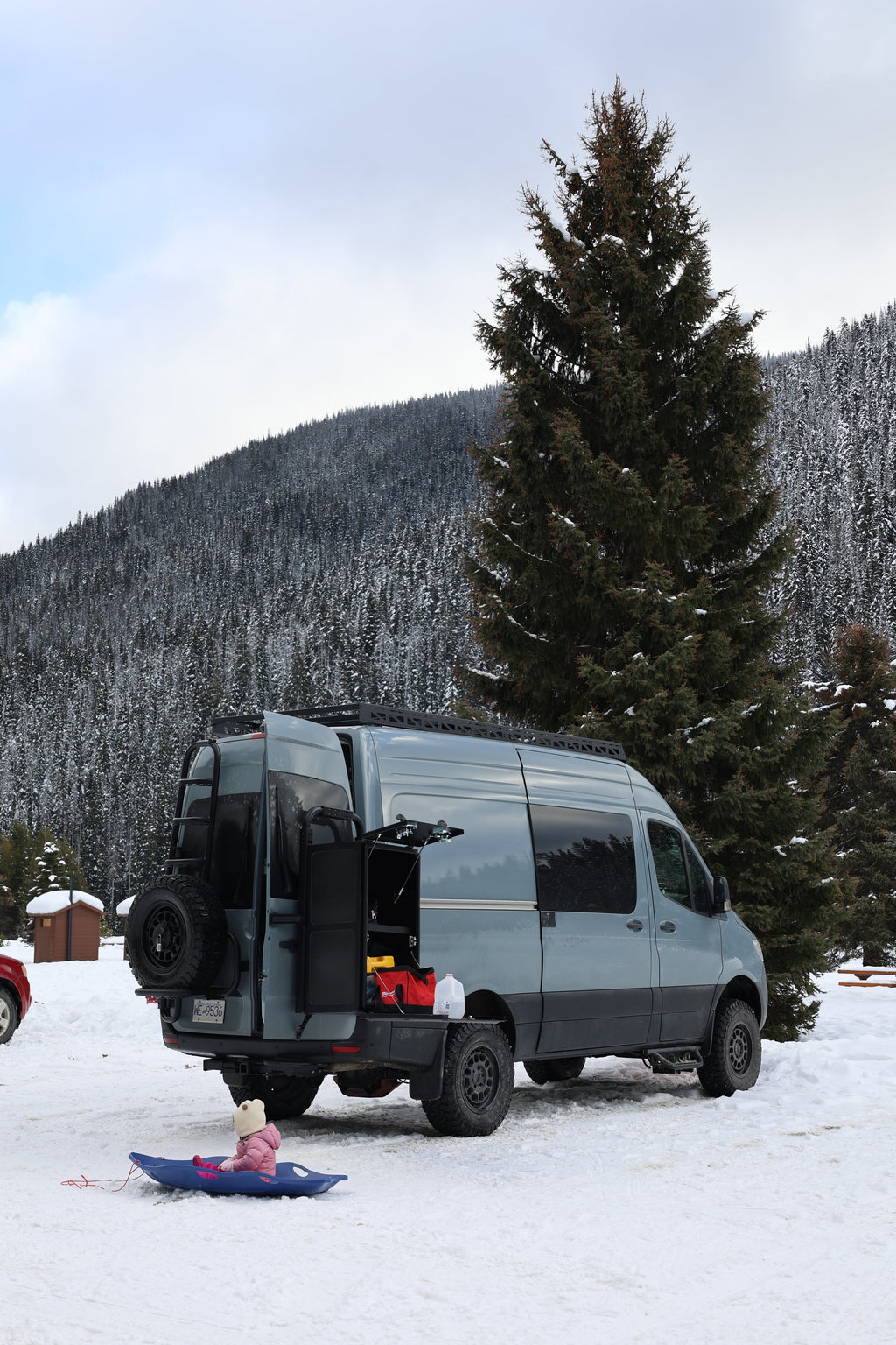 Van parked in a snowy landscape with mountains and trees in the background
