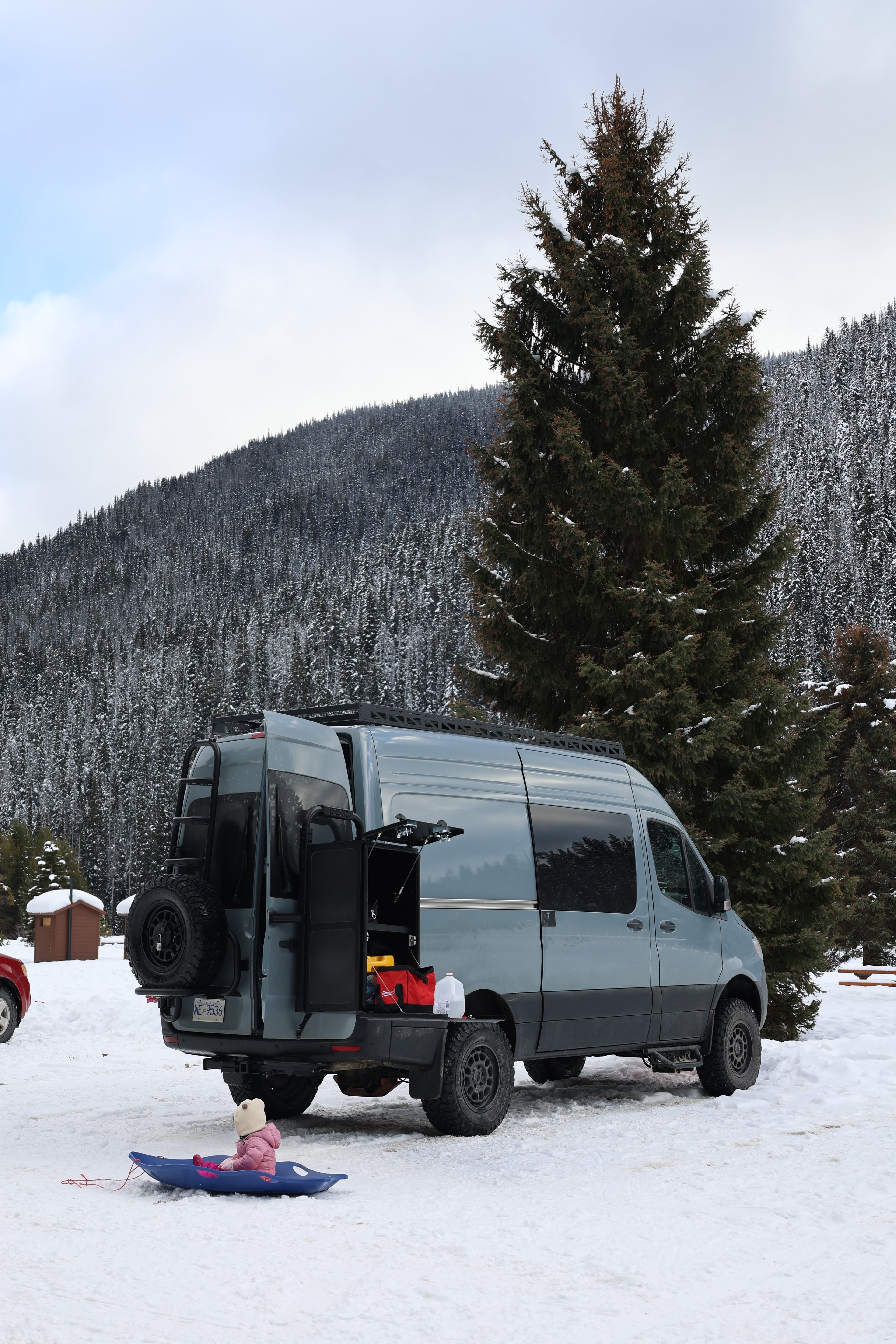 Van parked in a snowy landscape with mountains and trees in the background