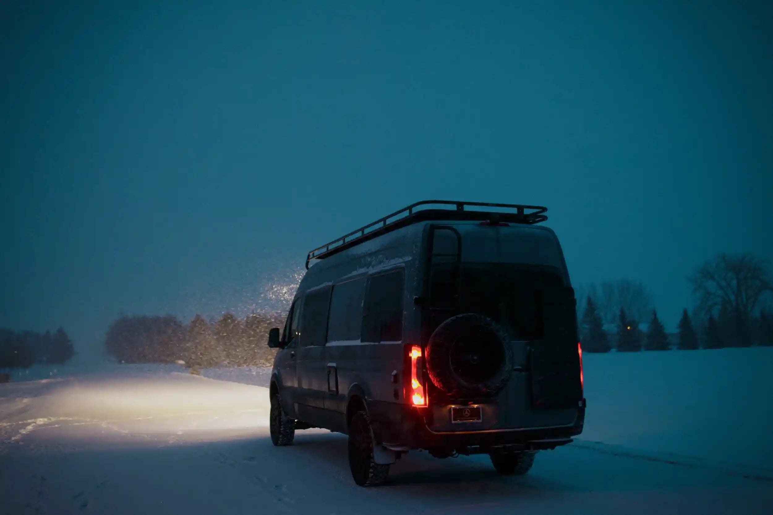 Van driving on a snowy road at night with headlights and brake lights on